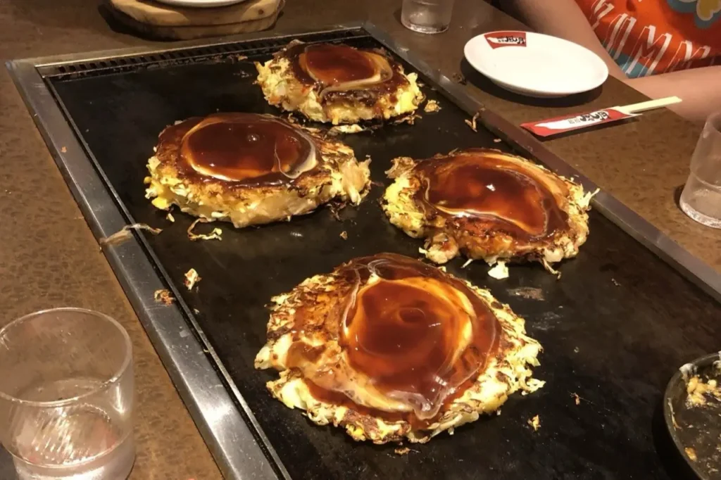 Okonomiyaki tra i piatti tipici giapponesi cotti sulla piastra con salsa